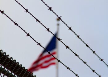 Barbed wire in the foreground with a blurred American flag in the background