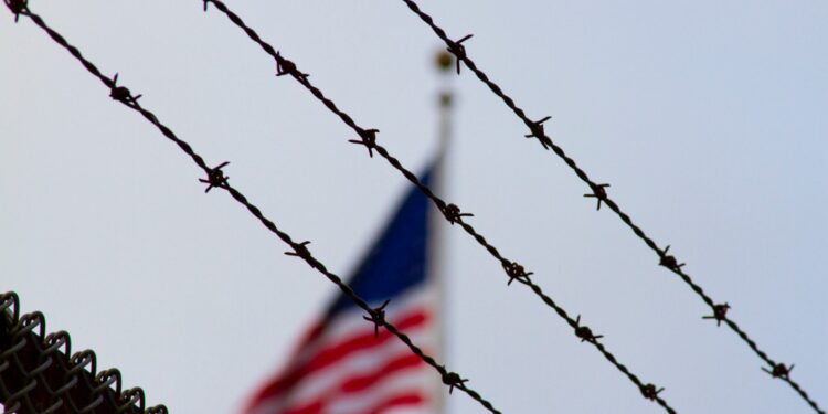 Barbed wire in the foreground with a blurred American flag in the background