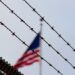 Barbed wire in the foreground with a blurred American flag in the background