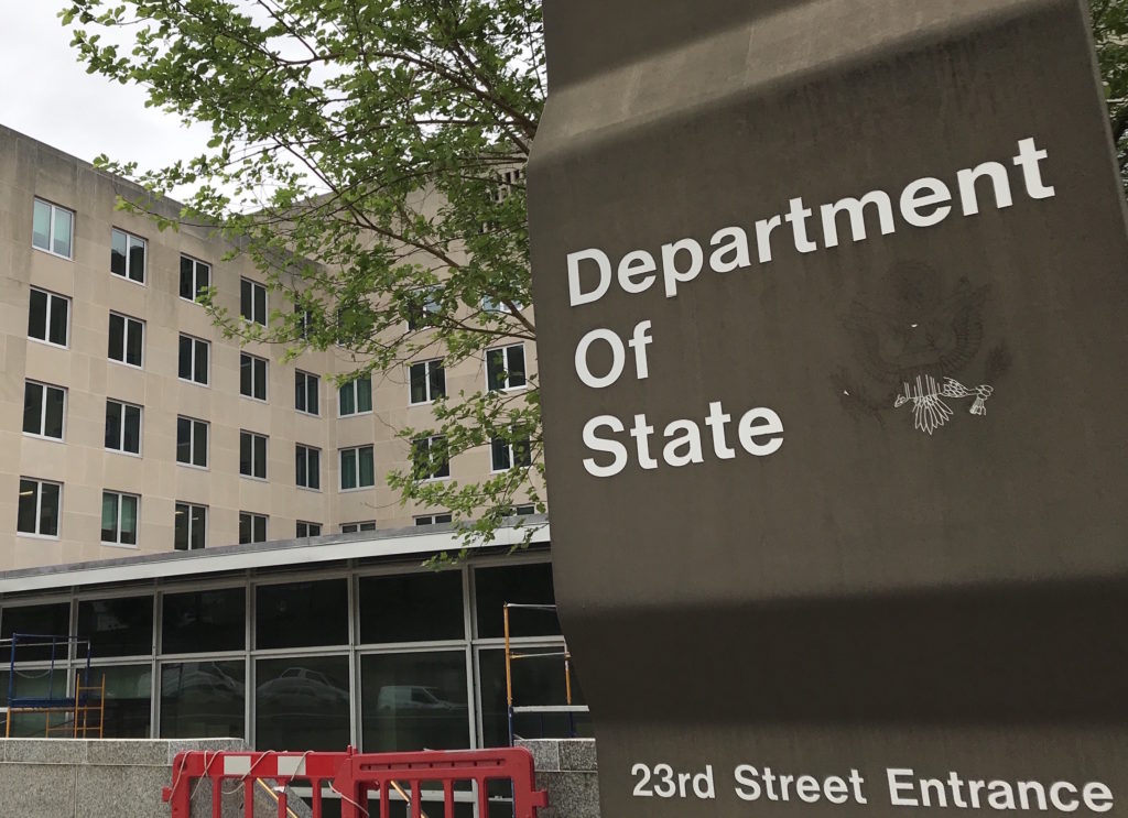 Photo of a sign for the Department of State in the foreground, with the building in the background