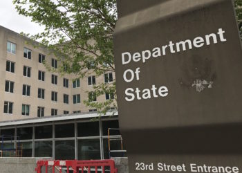 Photo of a sign for the Department of State in the foreground, with the building in the background