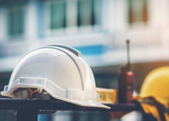 White safety helmet in the foreground, yellow safety helmet in background, walkie-talkie between the helmets