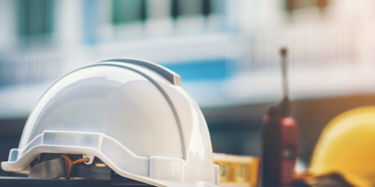 White safety helmet in the foreground, yellow safety helmet in background, walkie-talkie between the helmets