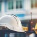 White safety helmet in the foreground, yellow safety helmet in background, walkie-talkie between the helmets