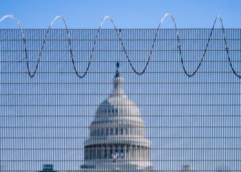 Photo of the U.S. Capitol building in the middle, with the blurry fence in the immediate foreground