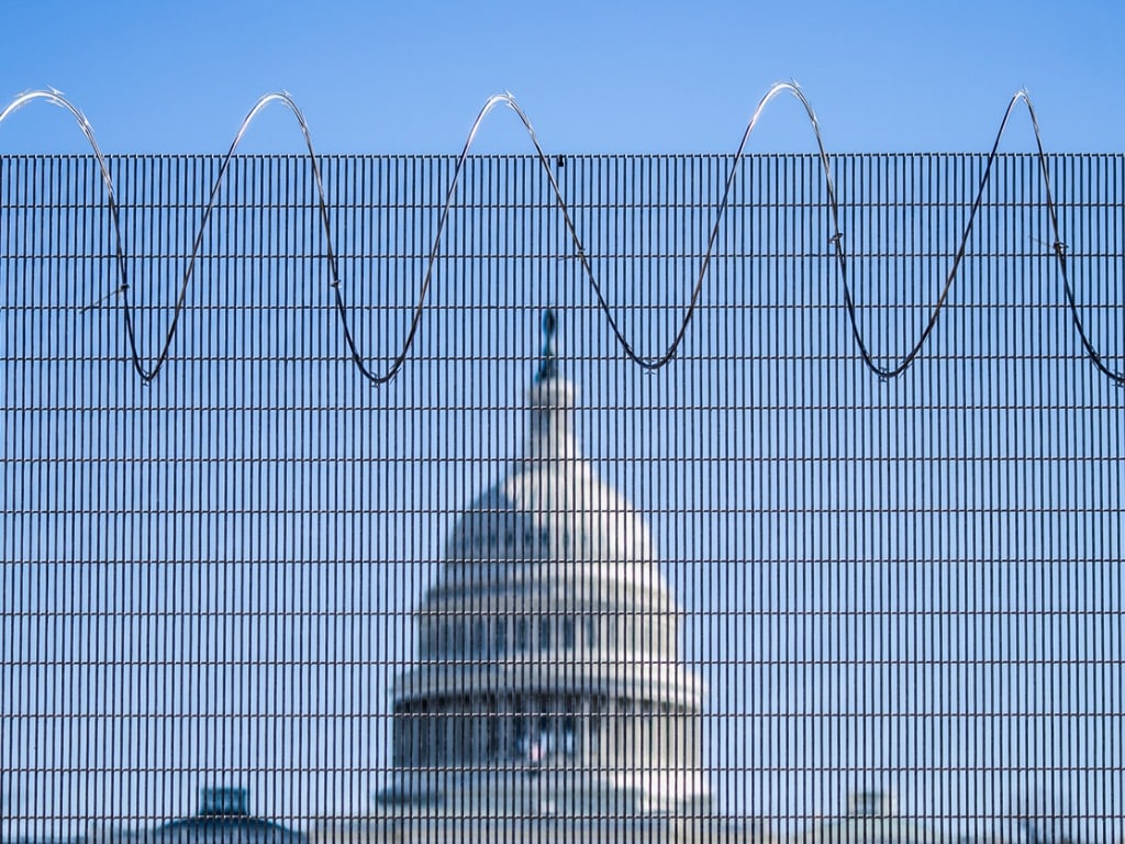 Photo of the U.S. Capitol building in the middle, with the blurry fence in the immediate foreground