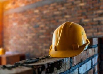 Photo of a yellow hard hat sitting on a brick wall being built, against a brick wall background