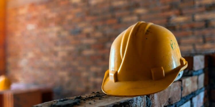 Photo of a yellow hard hat sitting on a brick wall being built, against a brick wall background