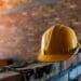 Photo of a yellow hard hat sitting on a brick wall being built, against a brick wall background