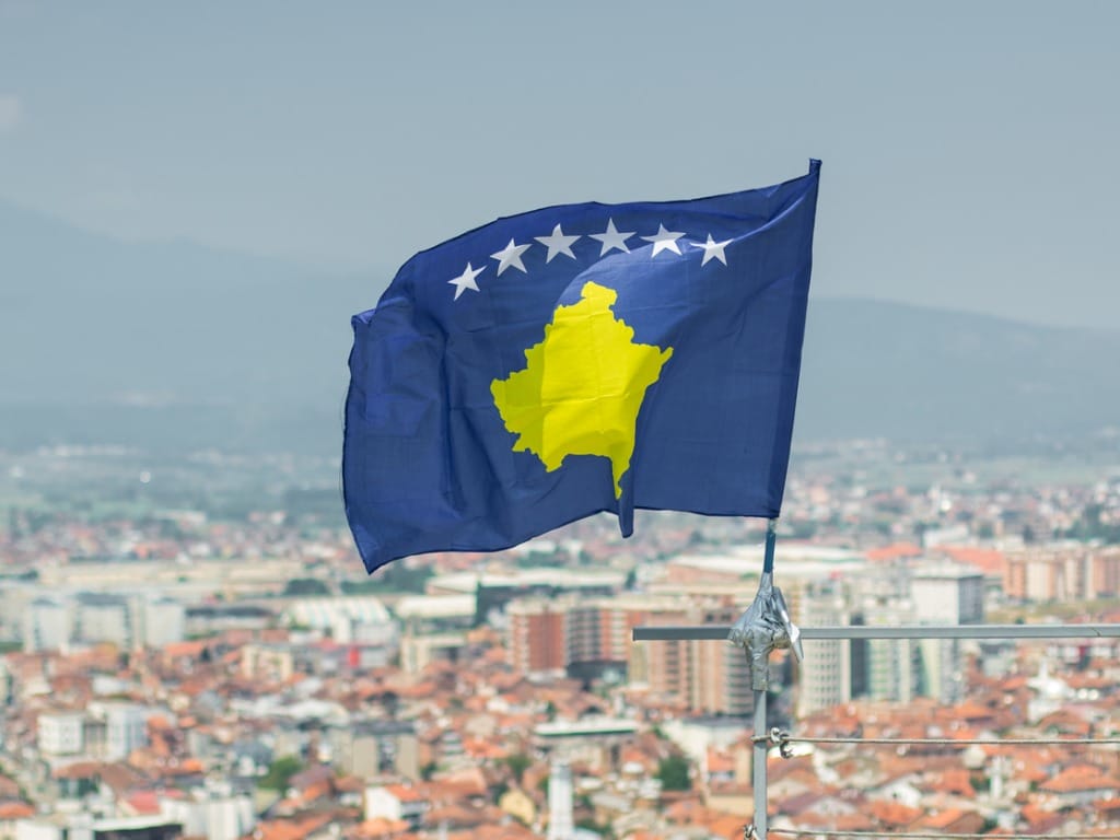 Photo of the Kosovo flag with a blurry picture of the city in the background