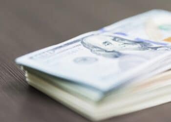 Close-up photo of a stack of $100 bills against a wooden surface