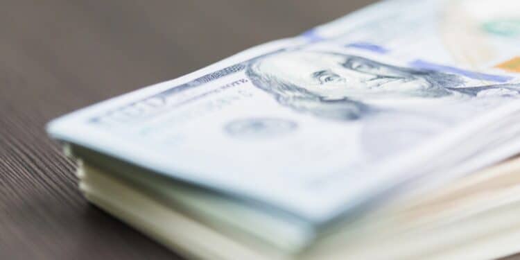 Close-up photo of a stack of $100 bills against a wooden surface