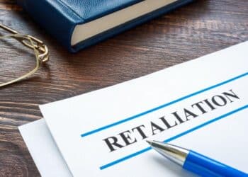Photo of a paper on a desk that says "RETALIATION" with a pen and book on the desk, too.