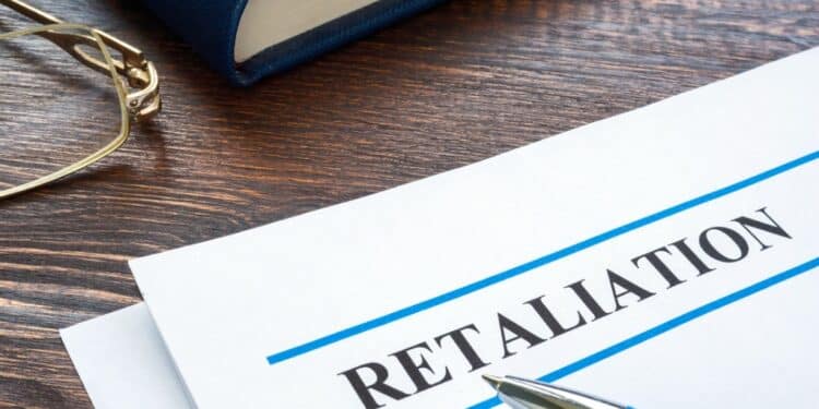 Photo of a paper on a desk that says "RETALIATION" with a pen and book on the desk, too.