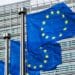Photo of three EU flags blowing in the wind in front of a building
