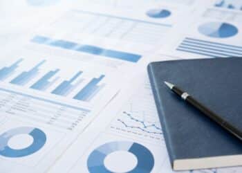 Photo of some blue charts and graphs with a notebook and pen on the righthand side