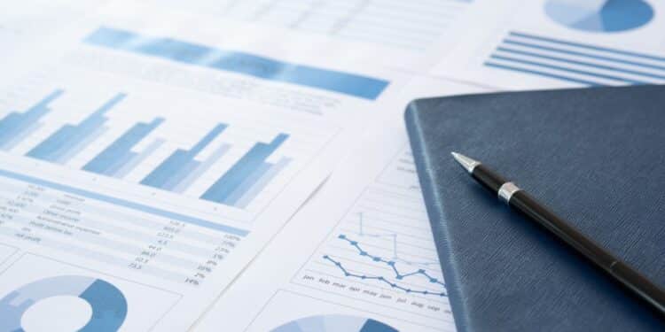Photo of some blue charts and graphs with a notebook and pen on the righthand side