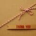Brown label with "Thank you" in red letters with a red and white string with a bow, all on a brown background