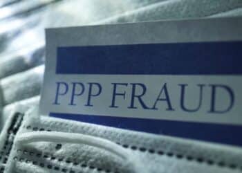A document with the words "PPP Fraud" laying on a medical facemask.
