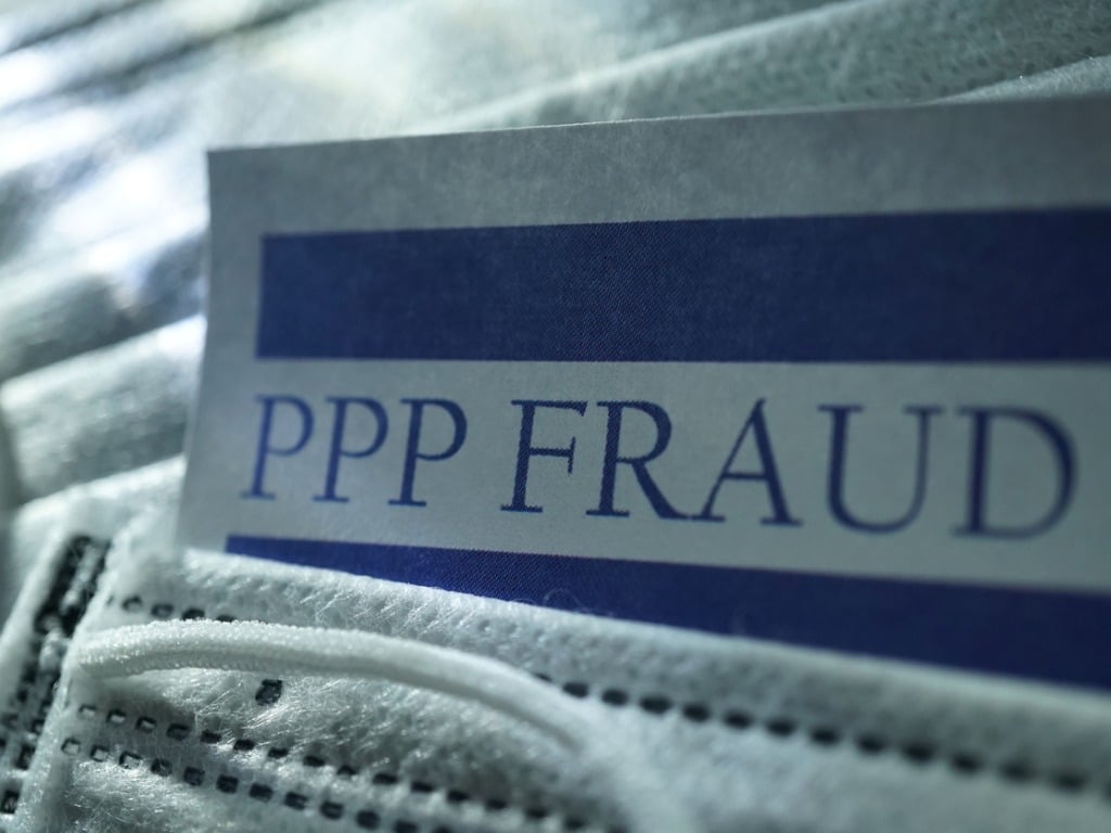 A document with the words "PPP Fraud" laying on a medical facemask.