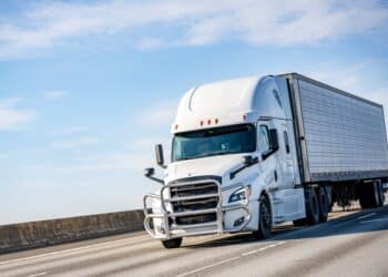 White semitruck driving on a road against a blue sky