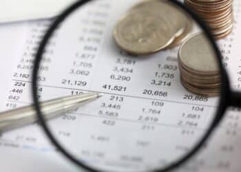 Financial documents under a magnifying glass with some change on the paper.