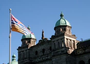 Photo of the B.C. parliament with the B.C. flag in the foreground