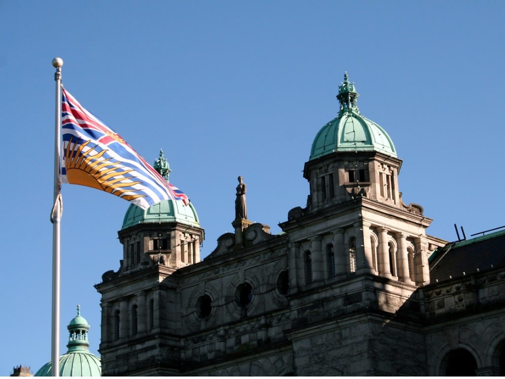 Photo of the B.C. parliament with the B.C. flag in the foreground