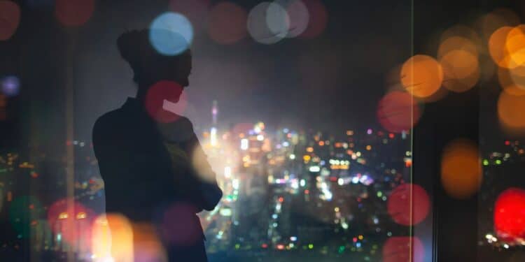 Silhouette of a young woman standing in a building overlooking city lights
