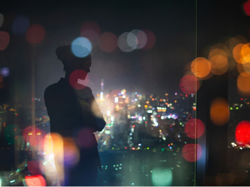 Silhouette of a young woman standing in a building overlooking city lights