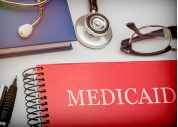 Red book with the words "Medicaid" on it and glasses and a stethoscope