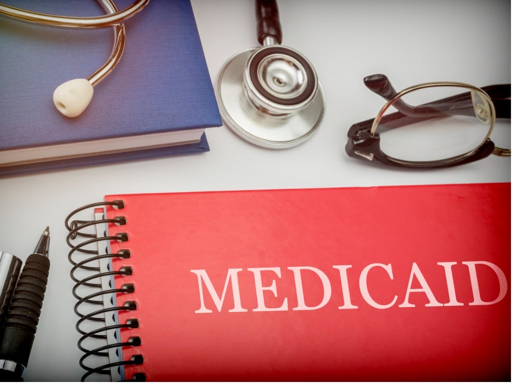 Red book with the words "Medicaid" on it and glasses and a stethoscope