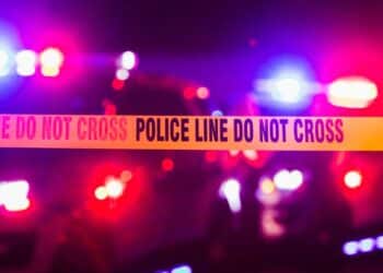 Crime scene tape that says "Police Line Do Not Cross" against blurry red and blue police lights