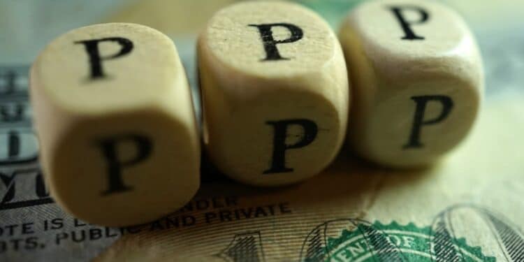 Wooden blocks spelling out "PPP" sitting on a dollar bill