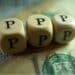 Wooden blocks spelling out "PPP" sitting on a dollar bill