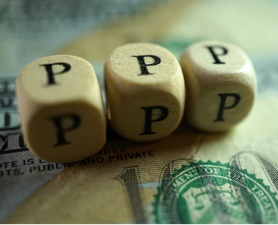 Wooden blocks spelling out "PPP" sitting on a dollar bill