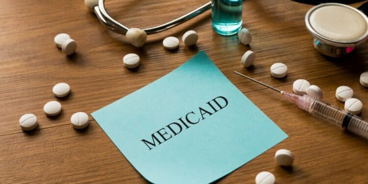Sticky note that says "Medicaid" surrounded by pills and a syringe on a wooden table