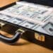 Attache filled with money sitting on a wooden table