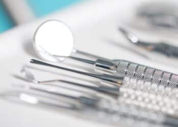 Row of silver dental instruments on a tray with a blurry background