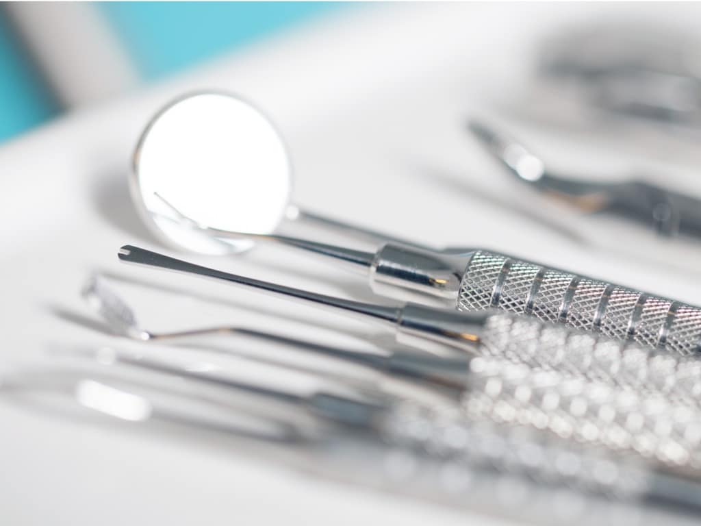 Row of silver dental instruments on a tray with a blurry background
