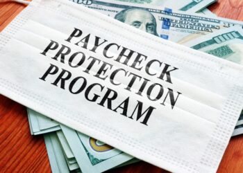 COVID-19 mask sitting on a pile of dollar bills with the words "Paycheck Protection Program" on it