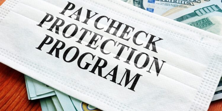 COVID-19 mask sitting on a pile of dollar bills with the words "Paycheck Protection Program" on it